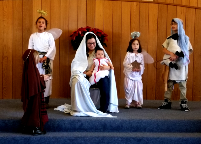 Singing angels, a shepherd, and a wise one gather around the mother and child.